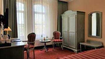 Quarto de hotel com uma cama, uma escrivaninha com luminária, duas cadeiras, um guarda-roupa e um espelho.