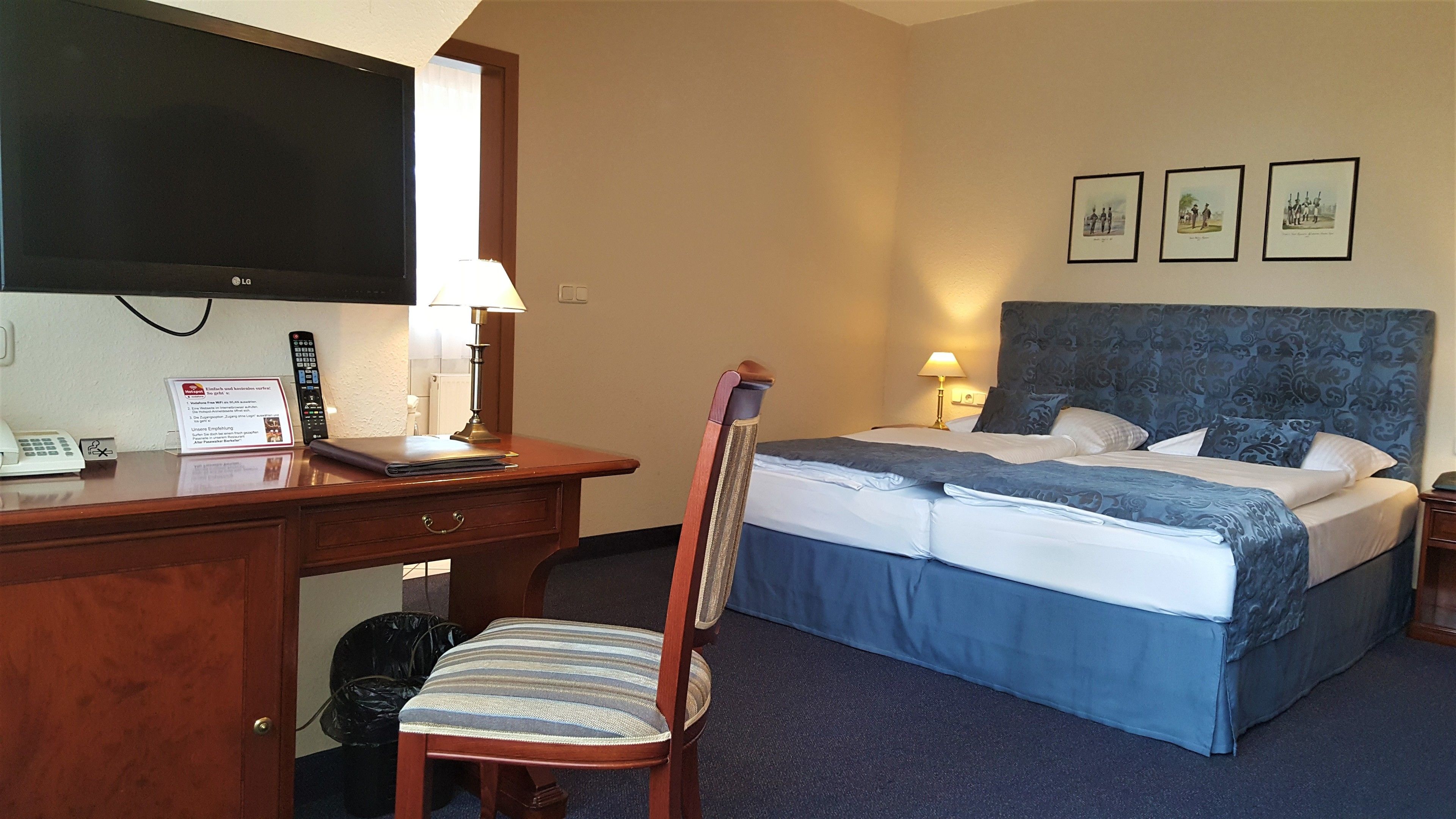 A hotel room with a bed, a desk with a lamp, a chair, and a TV.