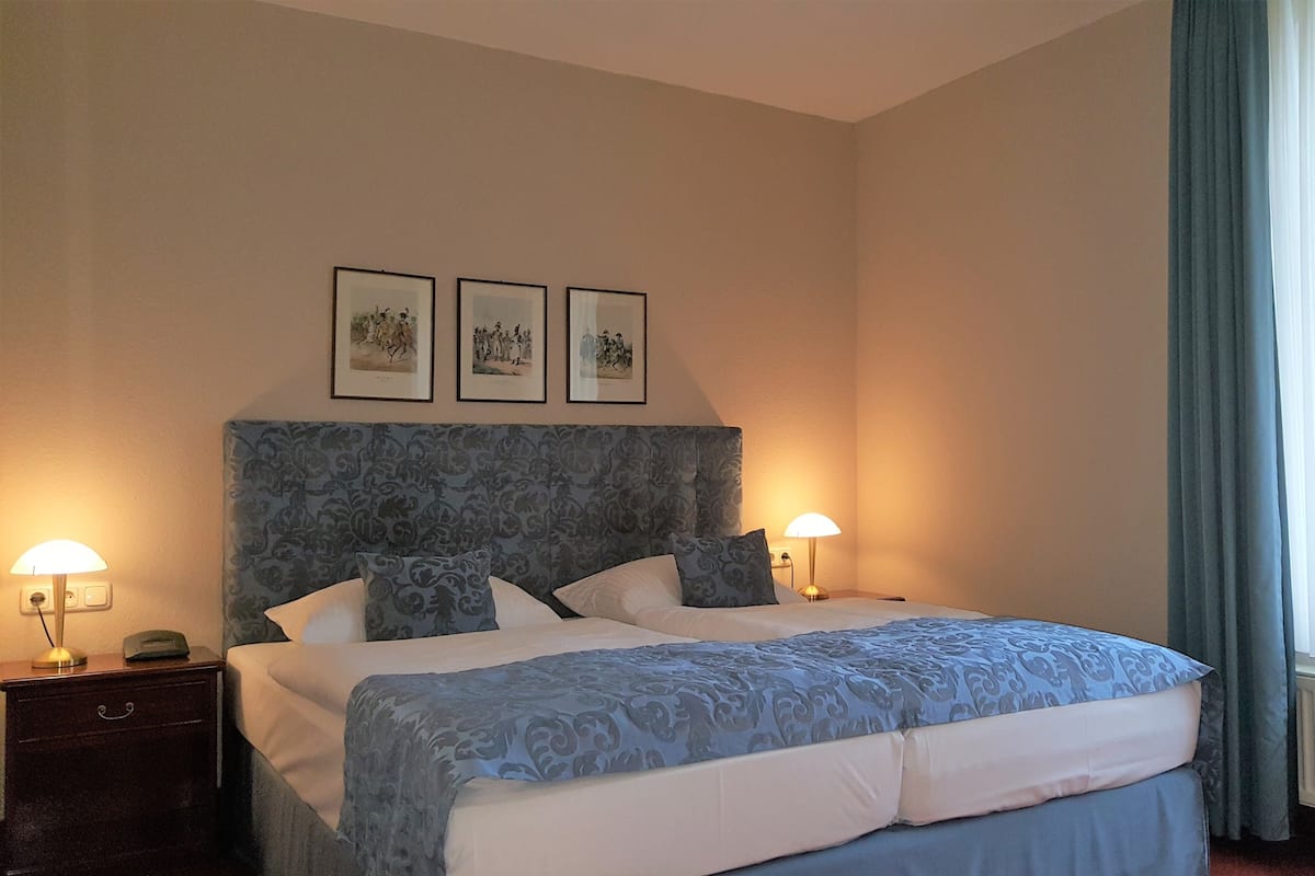 Habitación de hotel con una cama grande, dos mesitas de noche, un cabecero con diseño estampado y tres cuadros en la pared.