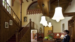 A hotel lobby with a wooden reception desk, a staircase with red carpet, and a chandelier. - Villa Knobelsdorff (Pasewalk)