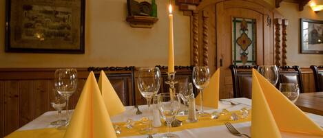 A dining table set with yellow napkins, wine glasses, and cutlery, with a candle centerpiece.