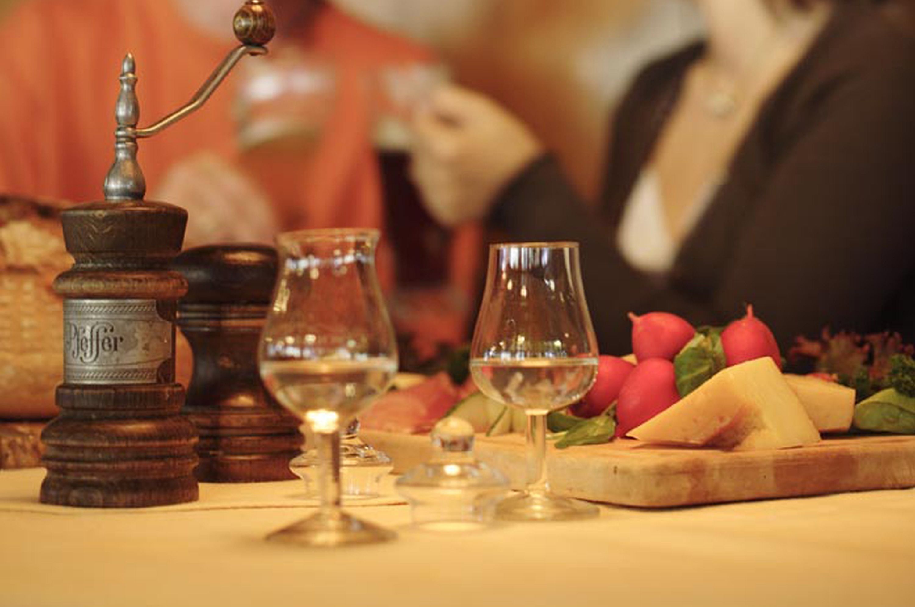 Une table en bois, sur laquelle on trouve une planche à fromage, des verres à vin et un moulin à poivre.