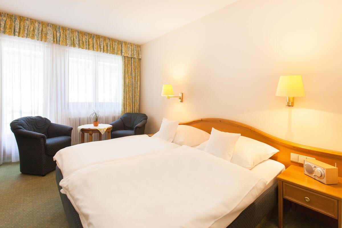 A hotel room with a large bed, two armchairs, a small table, and two bedside lamps.