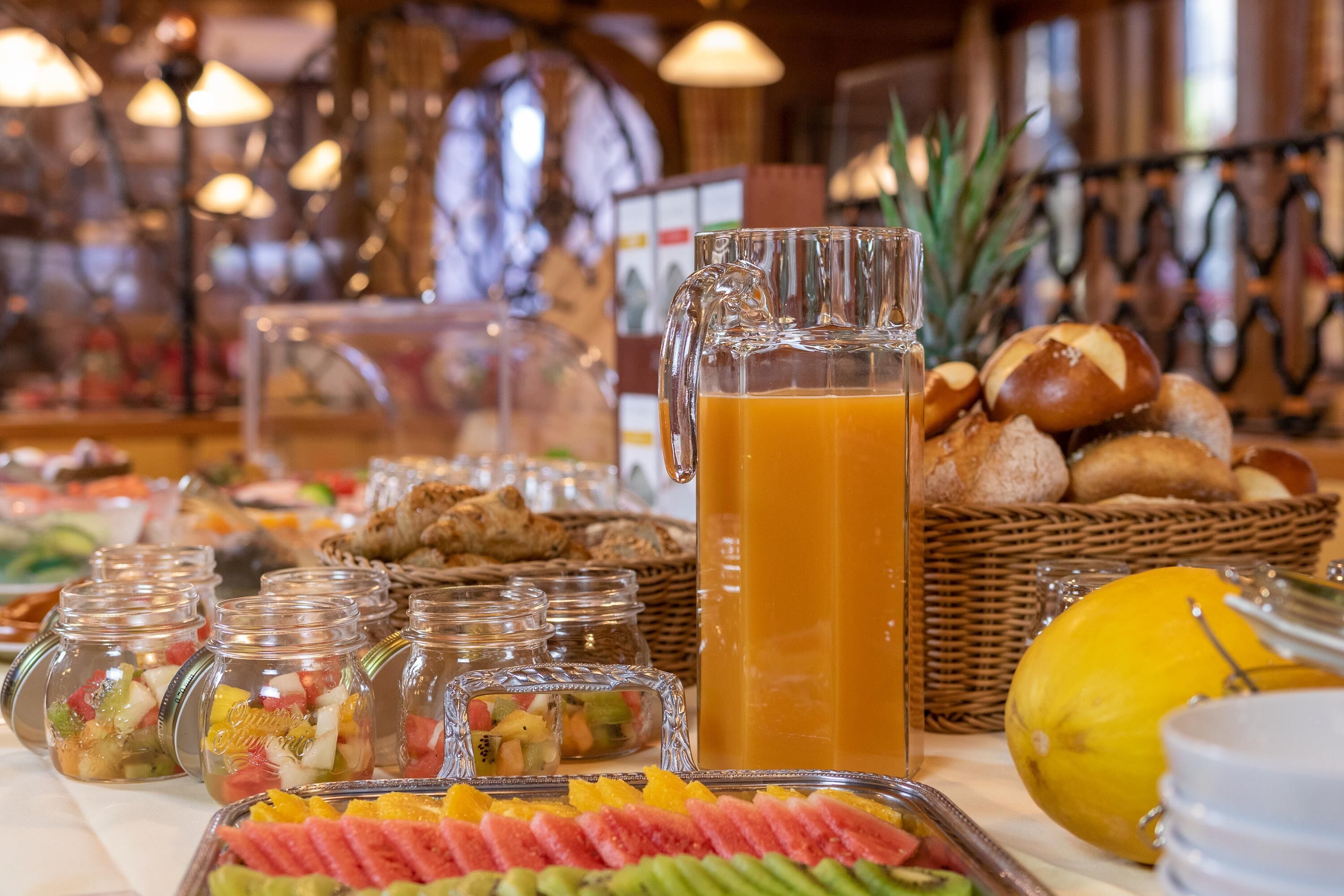 A buffet with various food items, including fruits, pastries, and a pitcher of orange juice.