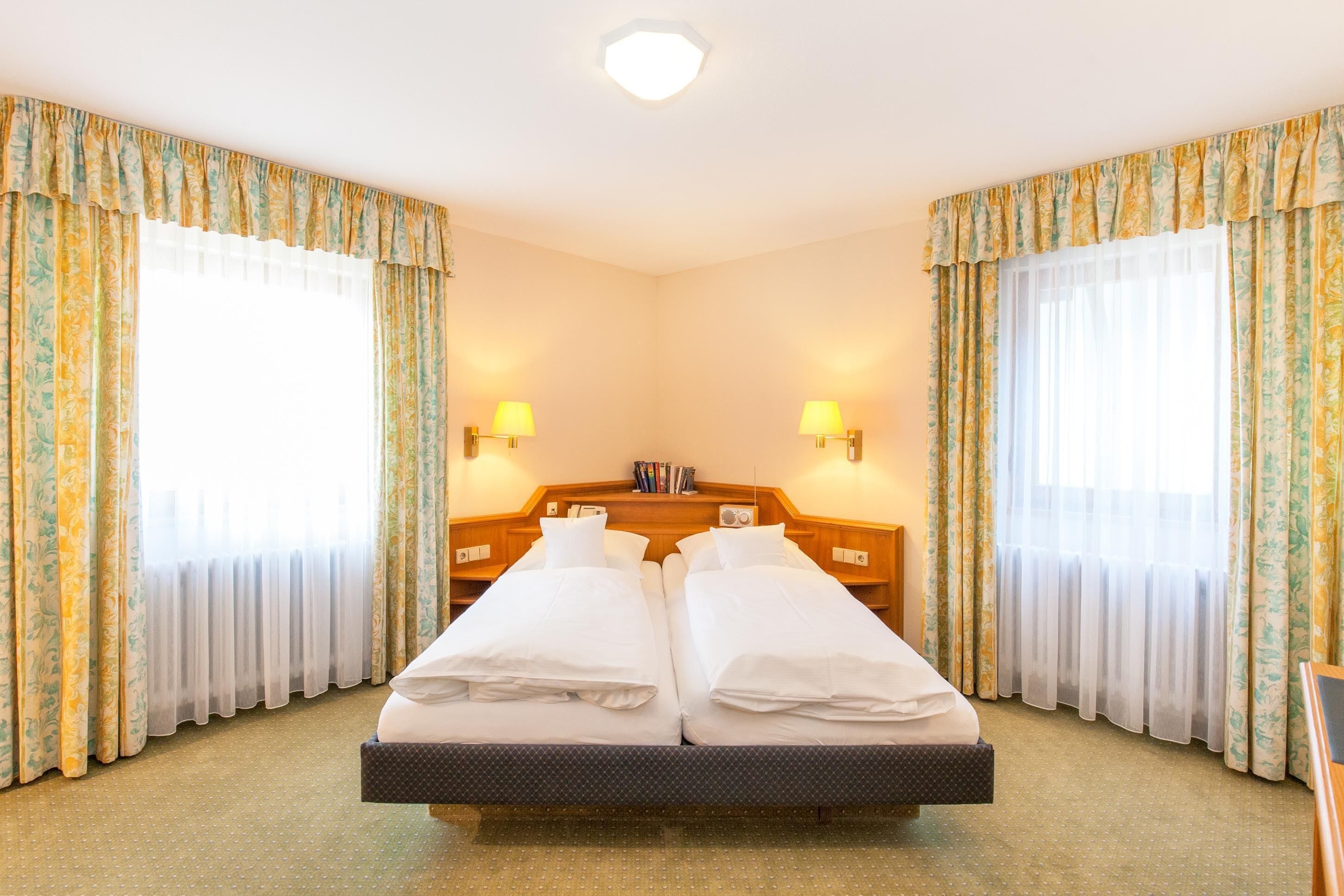 Un lit double avec deux oreillers, une tête de lit en bois, deux tables de chevet avec des lampes et une fenêtre avec des rideaux.