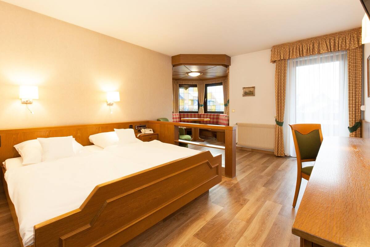 A hotel room with a wooden bed, a wooden desk, and a view of the city through large windows.