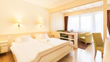 A hotel room with a large bed, two bedside lamps, a desk with a chair, and a window with curtains.