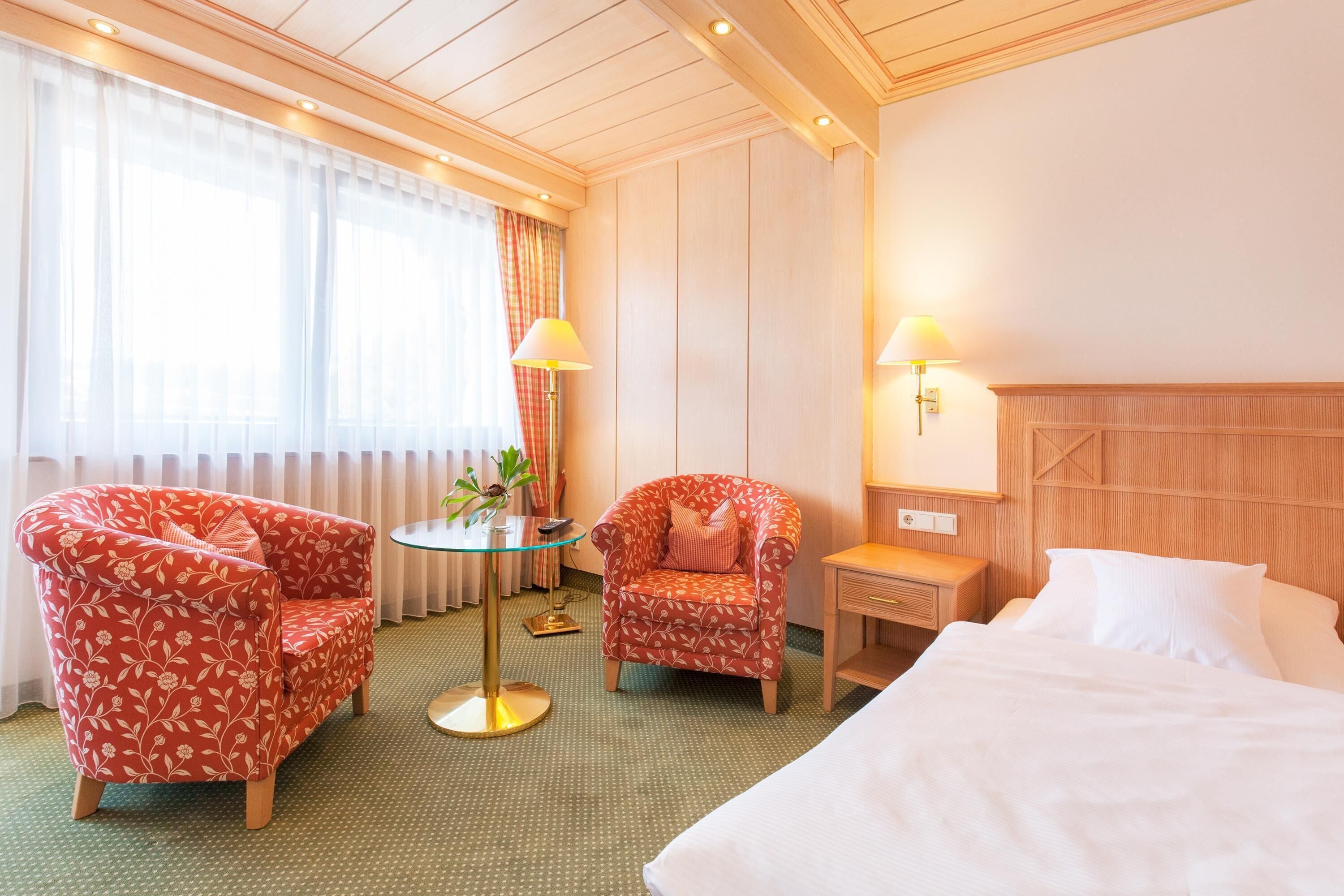 Una habitación de hotel con una cama, dos sillones, una mesita y una lámpara.