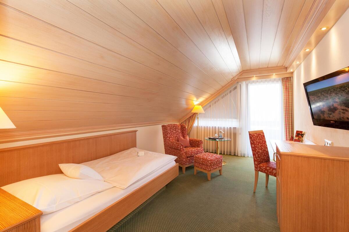 A hotel room with a wooden ceiling, a bed, a desk, a chair, and a television.