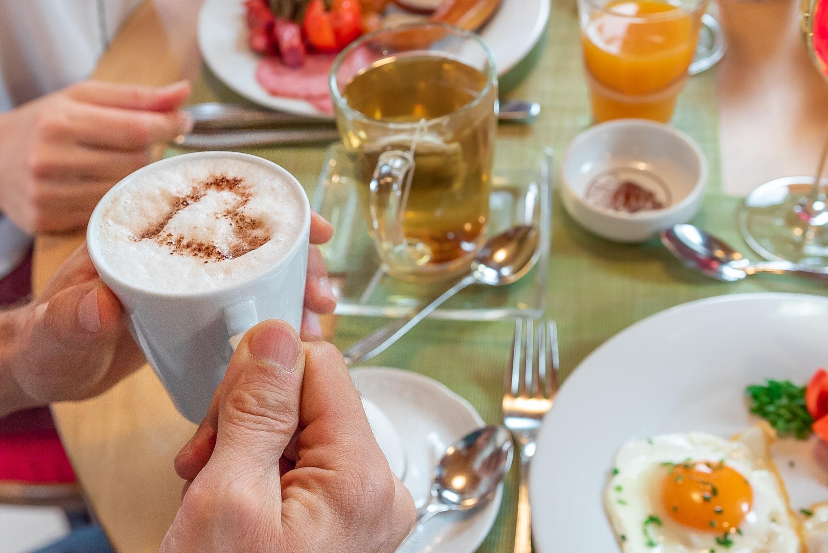 Una mesa de comedor con platos de comida, una taza de té y un vaso de zumo de naranja.