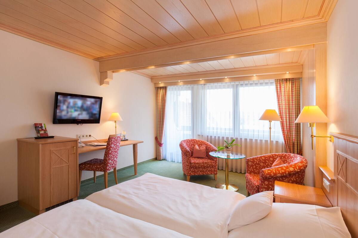 A hotel room with a bed, desk, chair, TV, and two lamps.