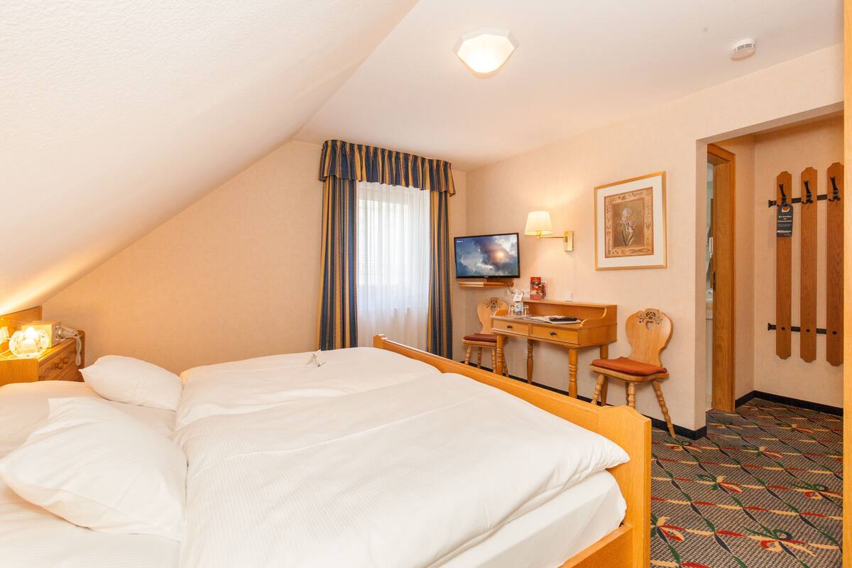 A hotel room with a large bed, a desk with a chair, a television, a framed picture on the wall, and a ski rack.