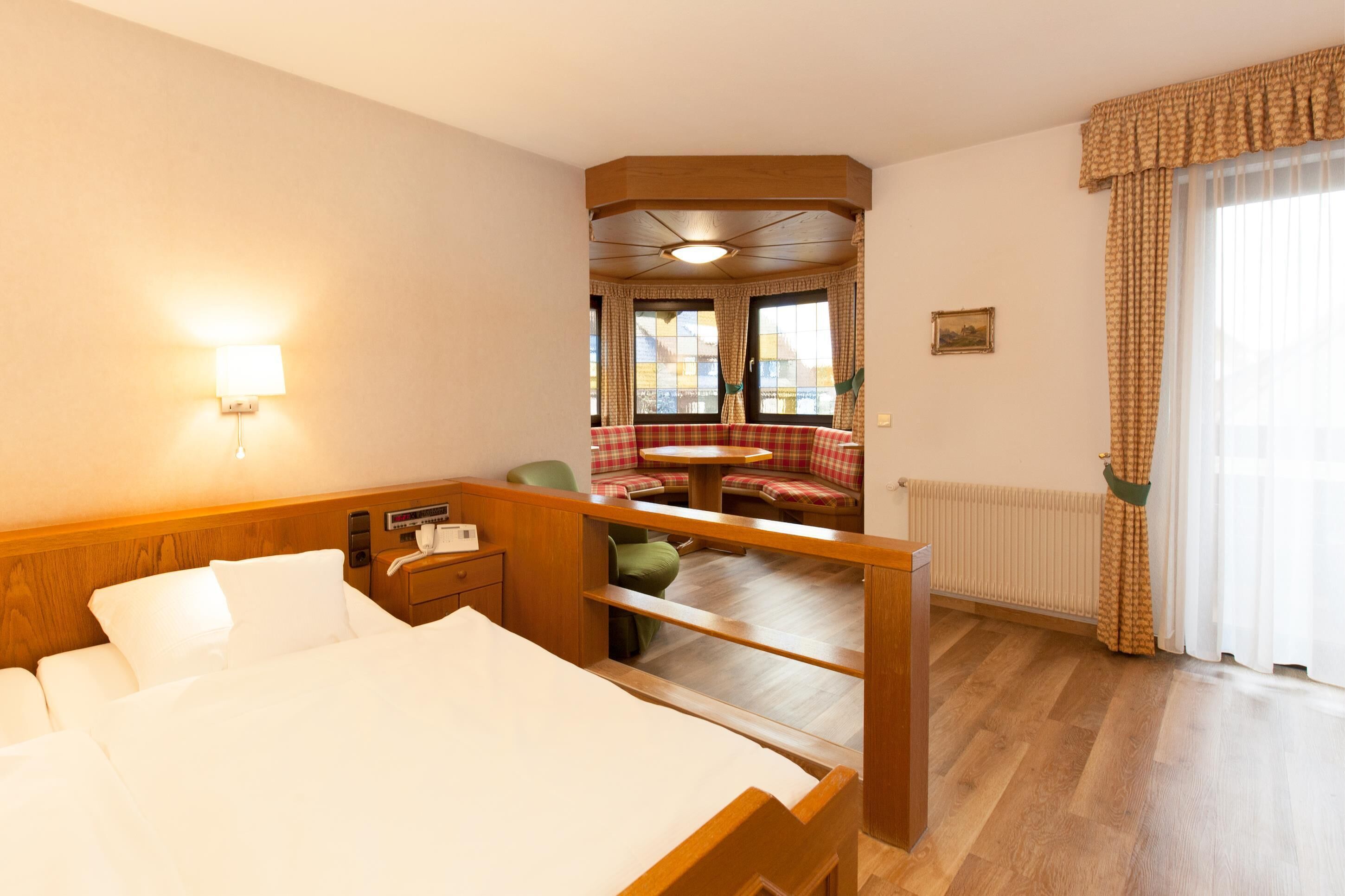 Une chambre d’hôtel avec un lit, une petite table, une chaise, une fenêtre avec des rideaux et une vue sur l’extérieur.