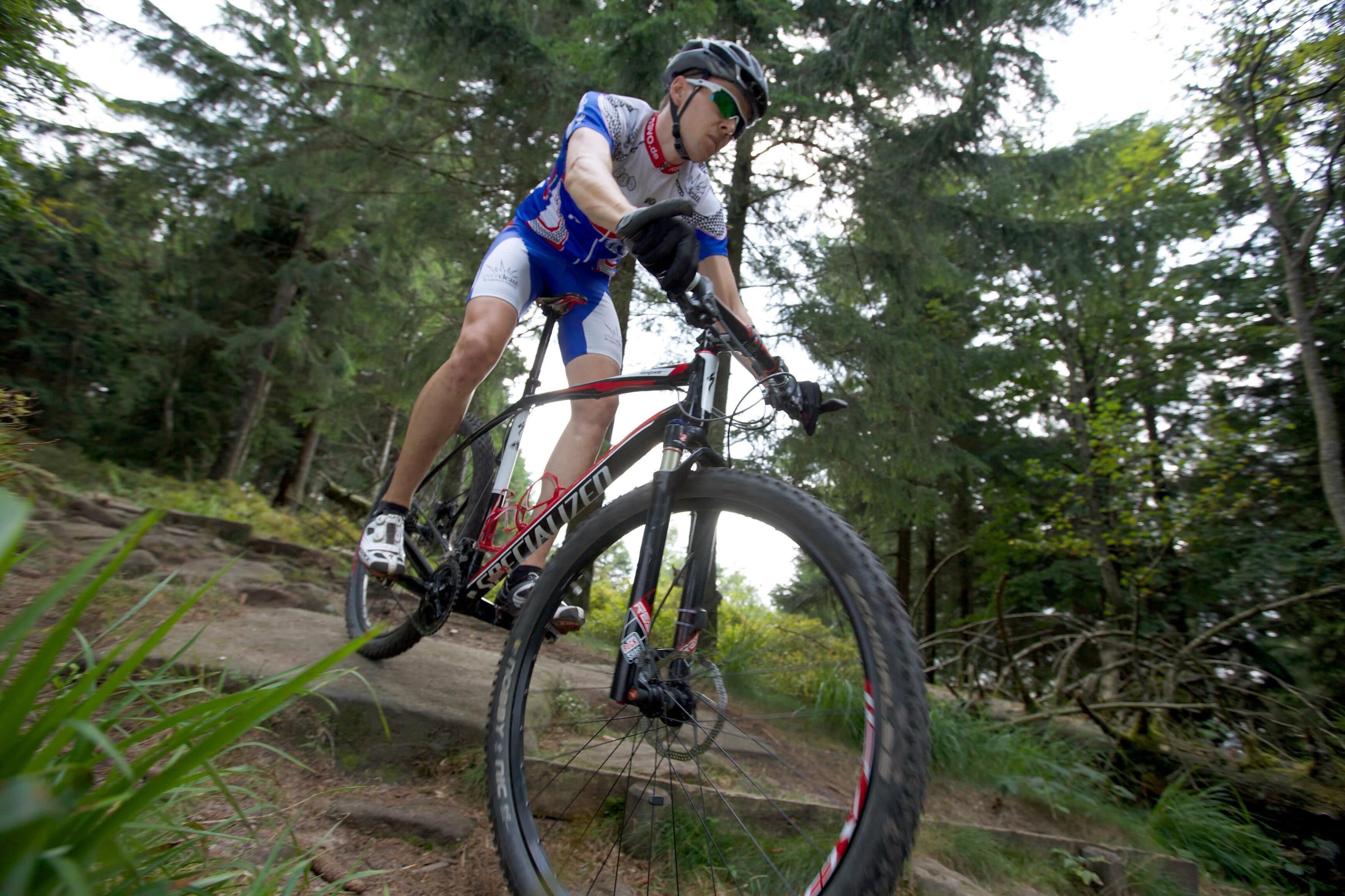 Un cycliste sur un sentier de montagne, à vélo tout-terrain, entouré d’arbres.