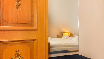 Eine Holztür mit floralen Schnitzereien, ein Bett mit weißen Leinen, eine Nachttischlampe und eine kleine Bank.