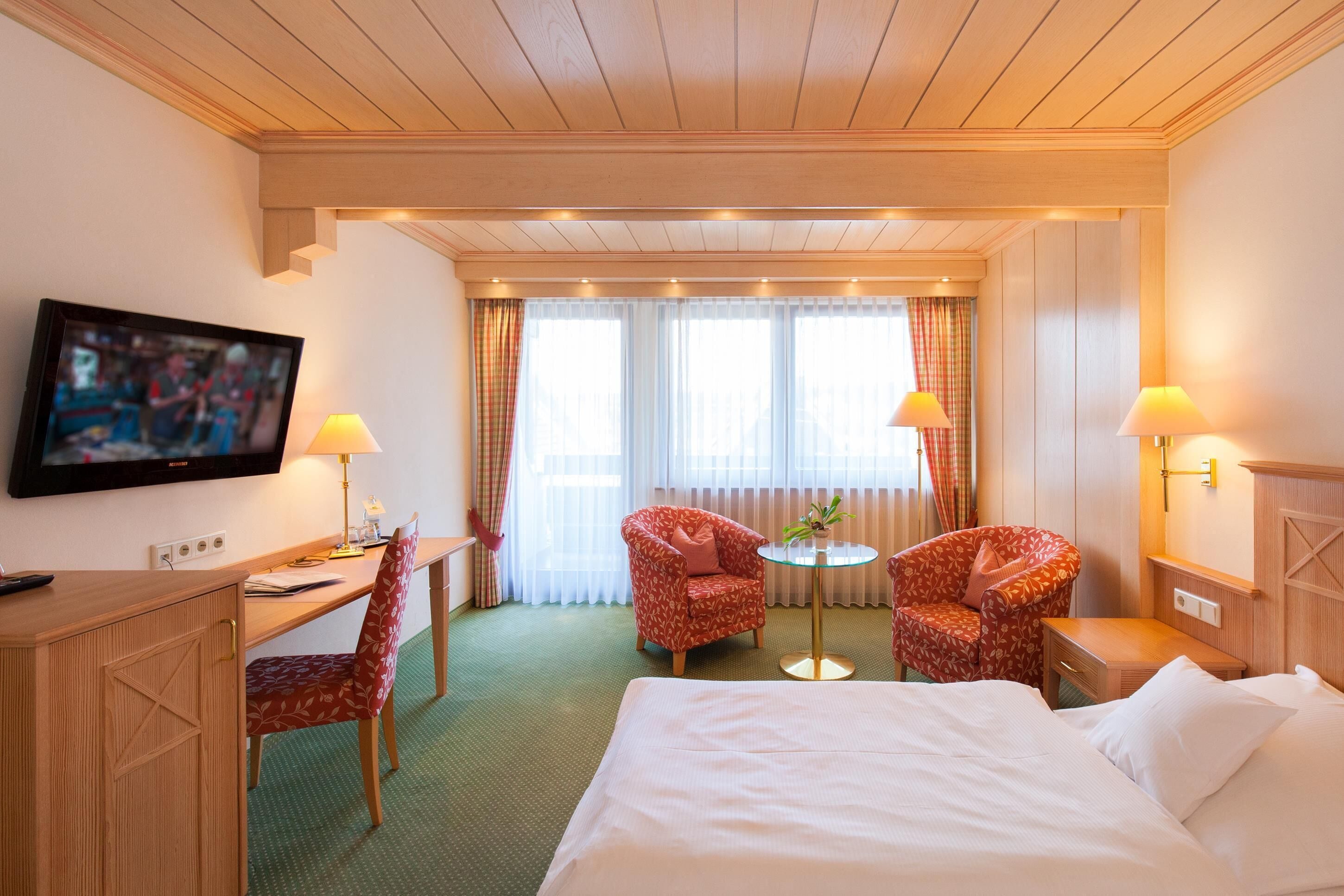 A hotel room with a bed, desk, chairs, TV, and a small table.