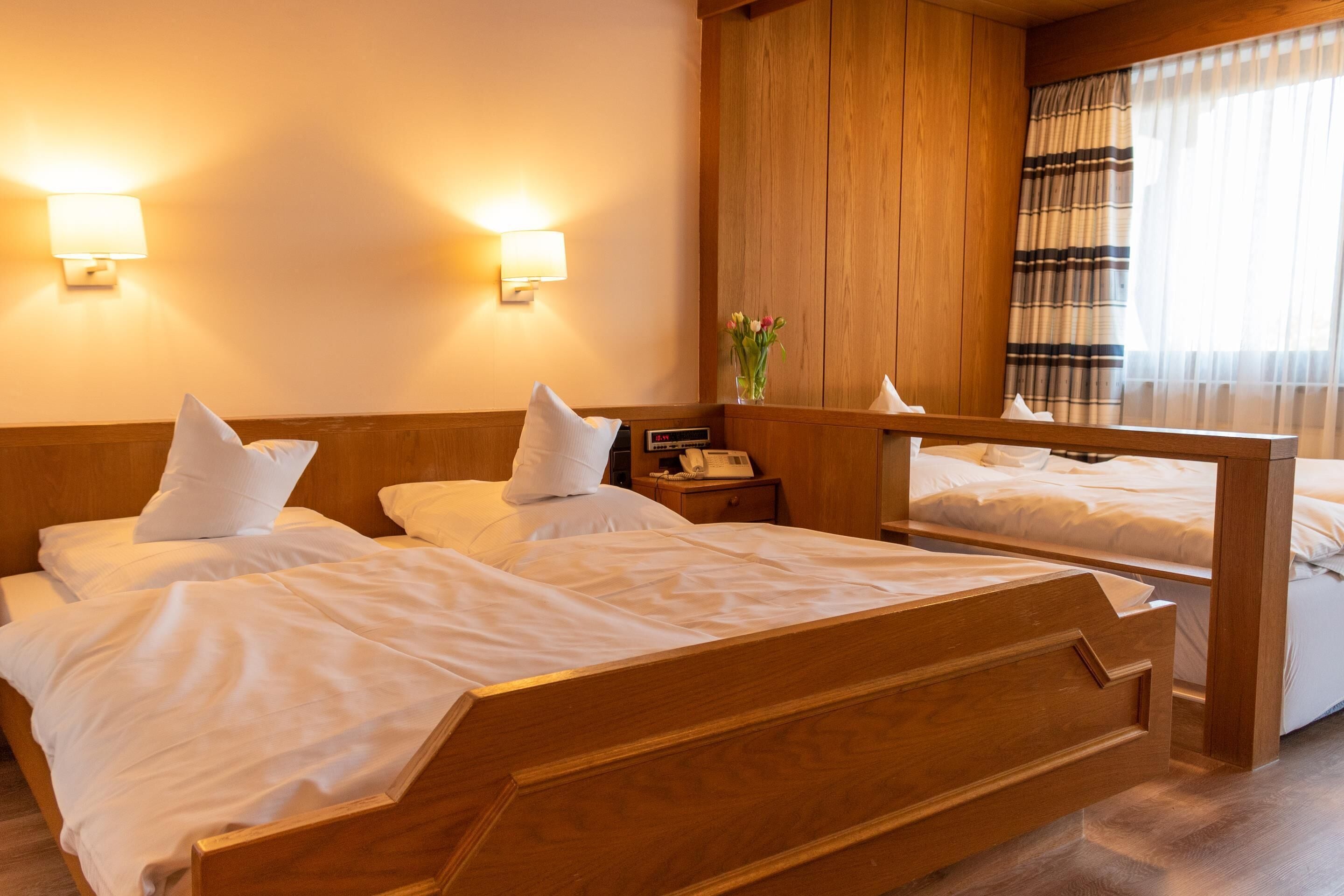 Une chambre d’hôtel avec deux lits en bois, une table de chevet avec un téléphone et un miroir au-dessus des lits.