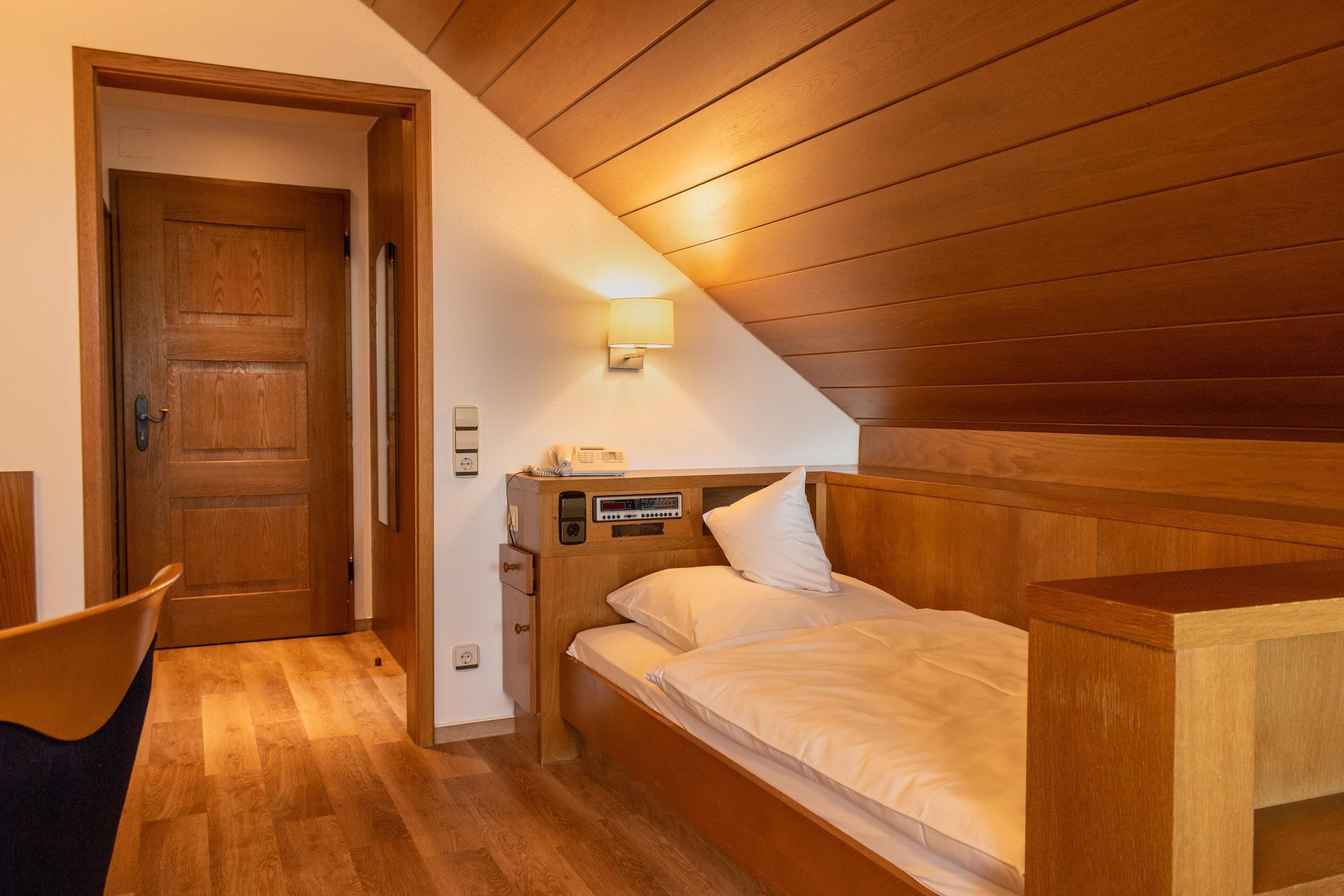 Ein Schlafzimmer mit Holzboden, einem Bett mit weißer Bettwäsche, einem Nachttisch und einer Wandlampe.