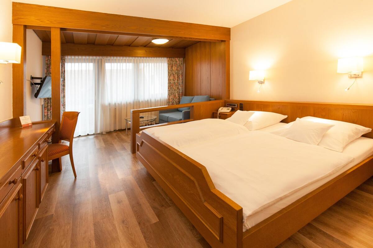 A hotel room with a wooden bed, a desk with a chair, a small table, and a television.