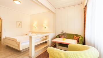 Una habitación con cama, una mesita con planta, una silla y una ventana con cortinas.