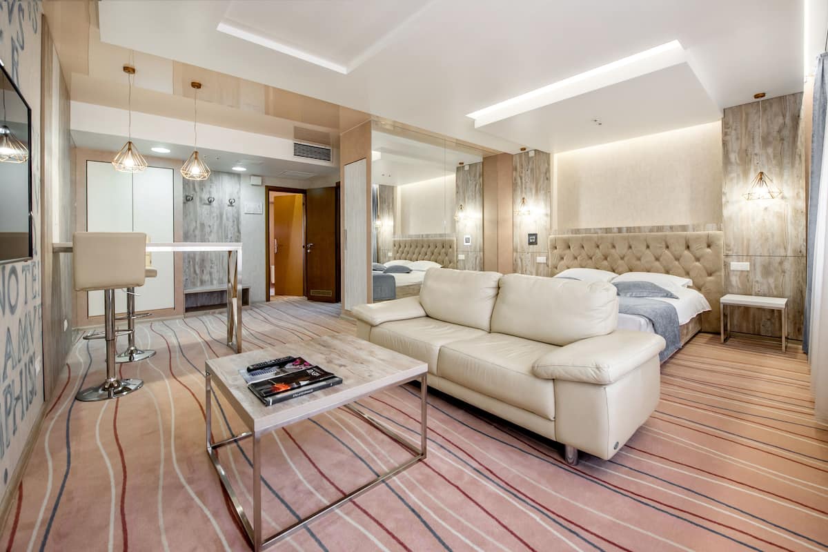 A modern hotel room with a large bed, a sofa, a coffee table, and a dining area.