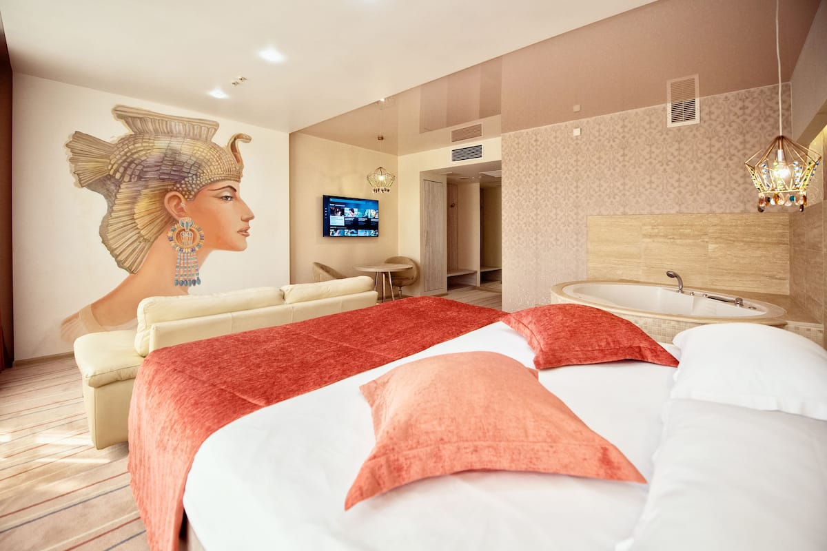 A modern hotel room with a large bed, a television, a bathroom with a bathtub, and a wall mural.