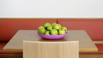 A dining area with a wooden table, a purple bowl of green apples, and a white pendant light with a blue shade.