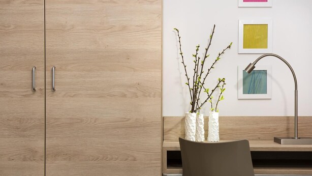 Une chambre moderne avec des meubles en bois, un bureau, une chaise et un vase décoré de branches.
