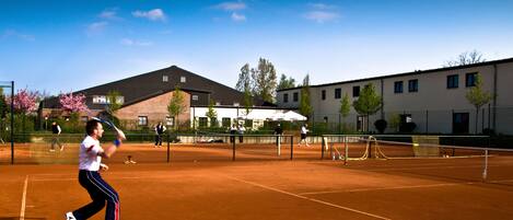 Una cancha de tenis con red, un edificio al fondo y cielo despejado.