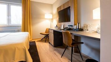 A hotel room with a bed, a desk with a chair, a television, and a window with curtains.