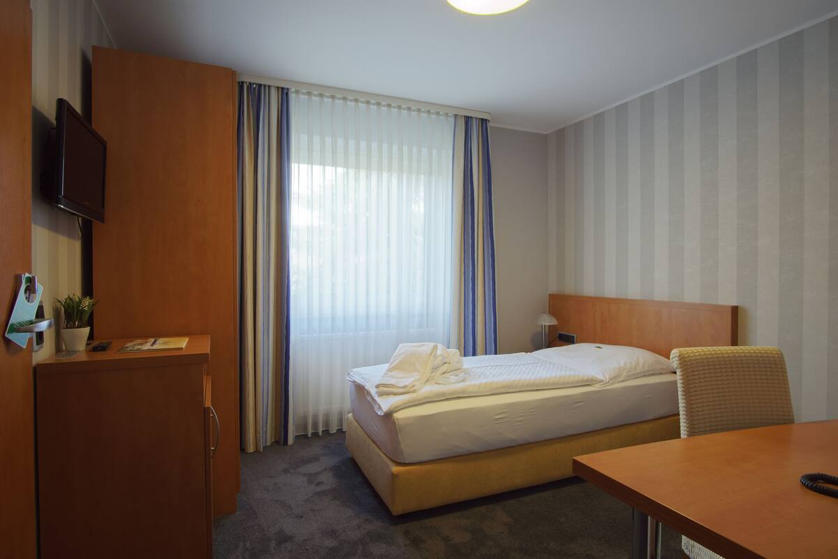 Ein Hotelzimmer mit Bett, Schreibtisch, Fernseher und einem Fenster mit Vorhängen.