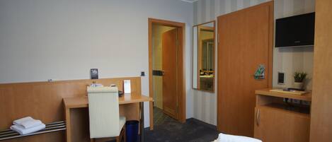 Quarto de hotel com cama, escrivaninha, cadeira, televisão e guarda-roupa.