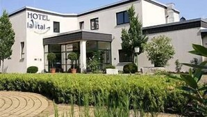 Un hôtel moderne à la façade blanche, doté de grandes fenêtres et d’un jardin bien entretenu à l’avant.