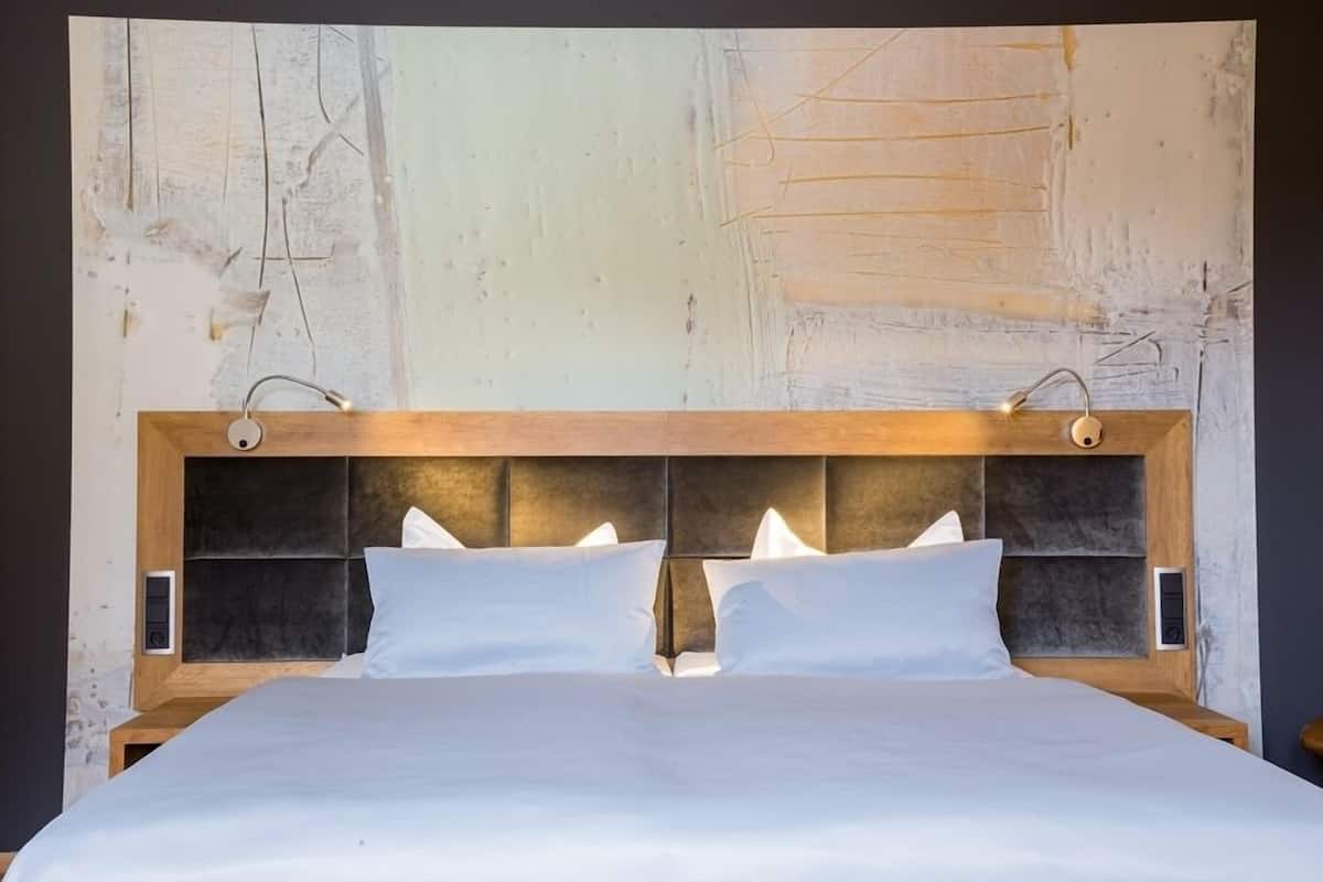 Ein Doppelbett mit Holz-Kopfteil, zwei Nachttische und ein großes abstraktes Gemälde an der Wand.