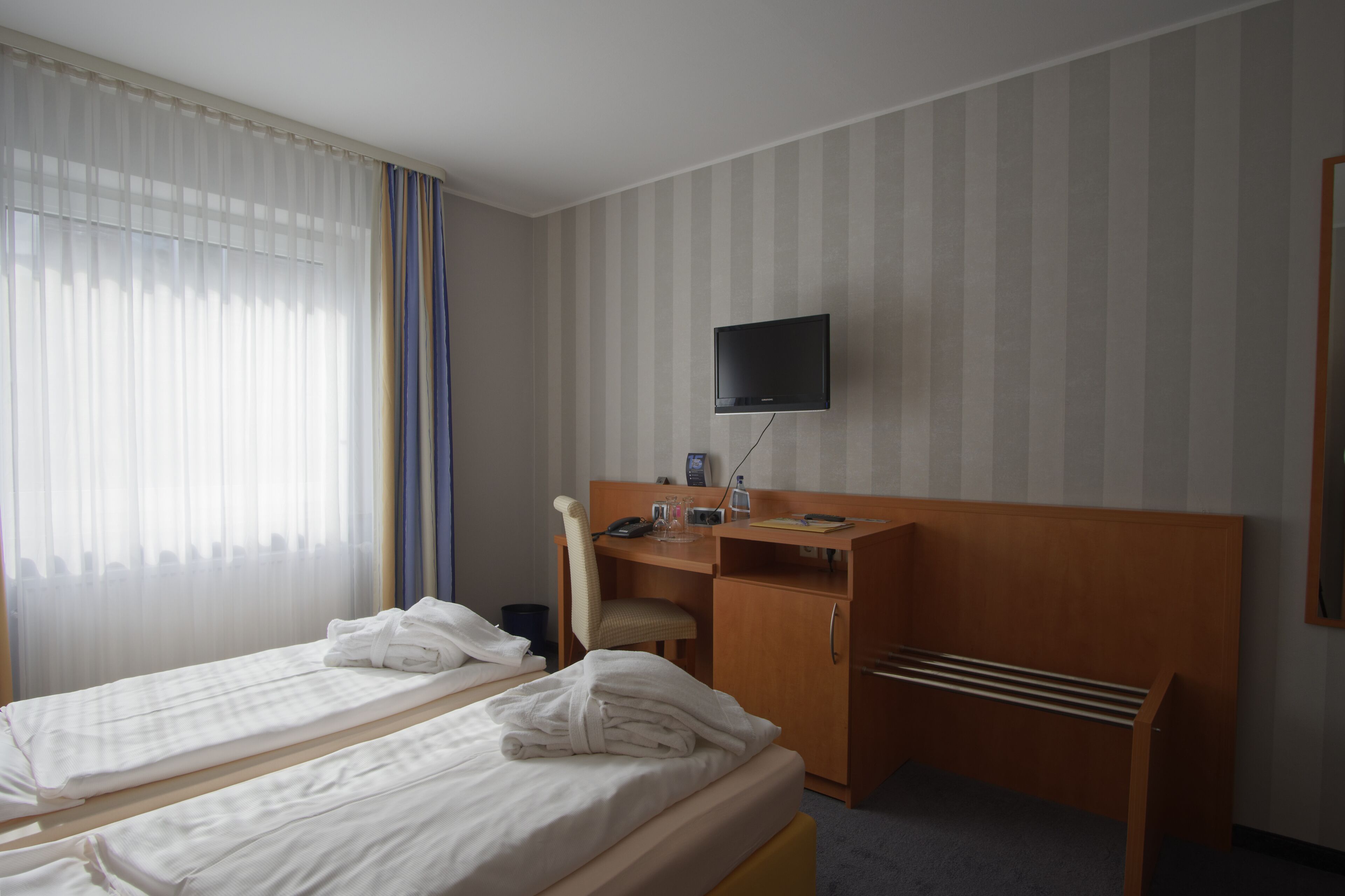 Habitación de hotel con dos camas, un escritorio, una silla, un televisor y una ventana con cortinas.