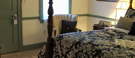 A bedroom with a four-poster bed, a nightstand, a lamp, and a window with curtains.