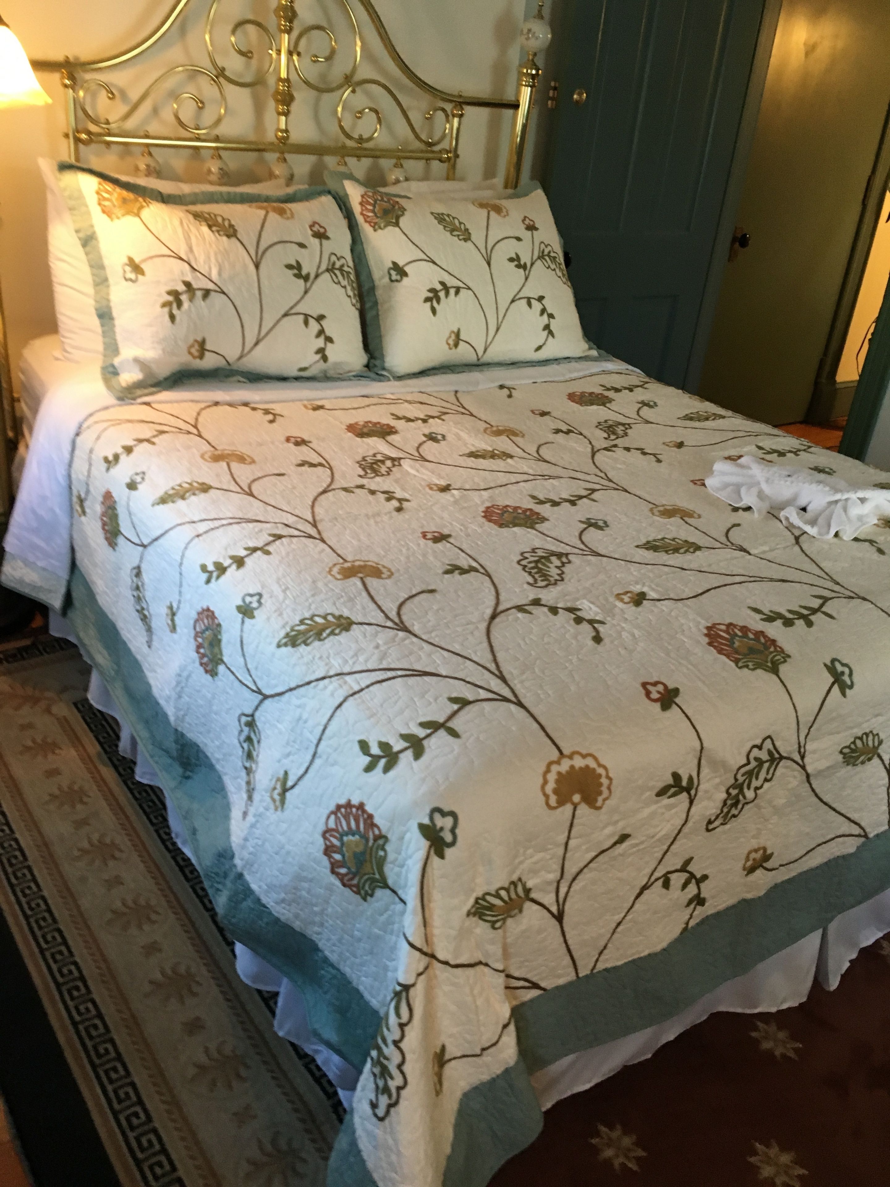 Uma cama com colcha estampada em flor, cabeceira de metal e mesa de cabeceira com abajur.