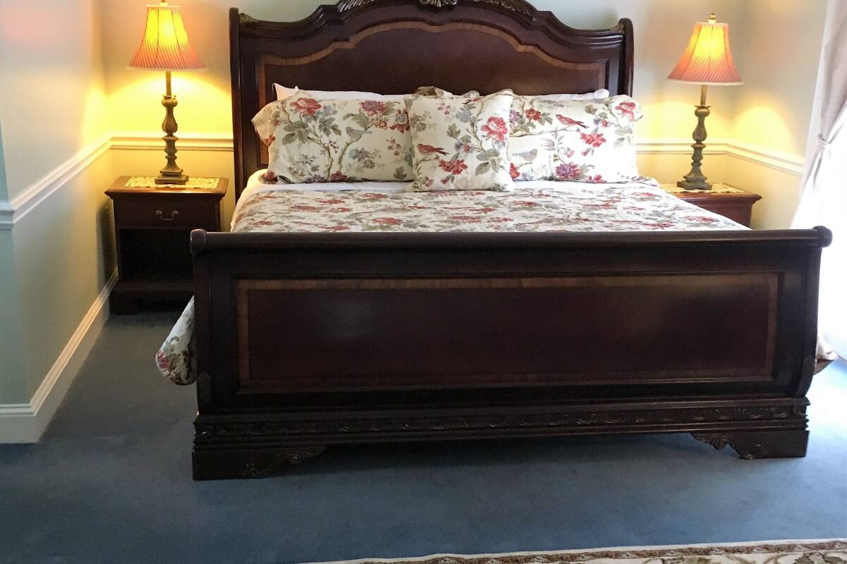 A bedroom with a wooden bed, floral bedding, two bedside lamps, and a patterned rug.