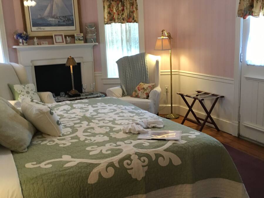 A bedroom with a bed, a chair, a lamp, a fireplace, and a ceiling fan.