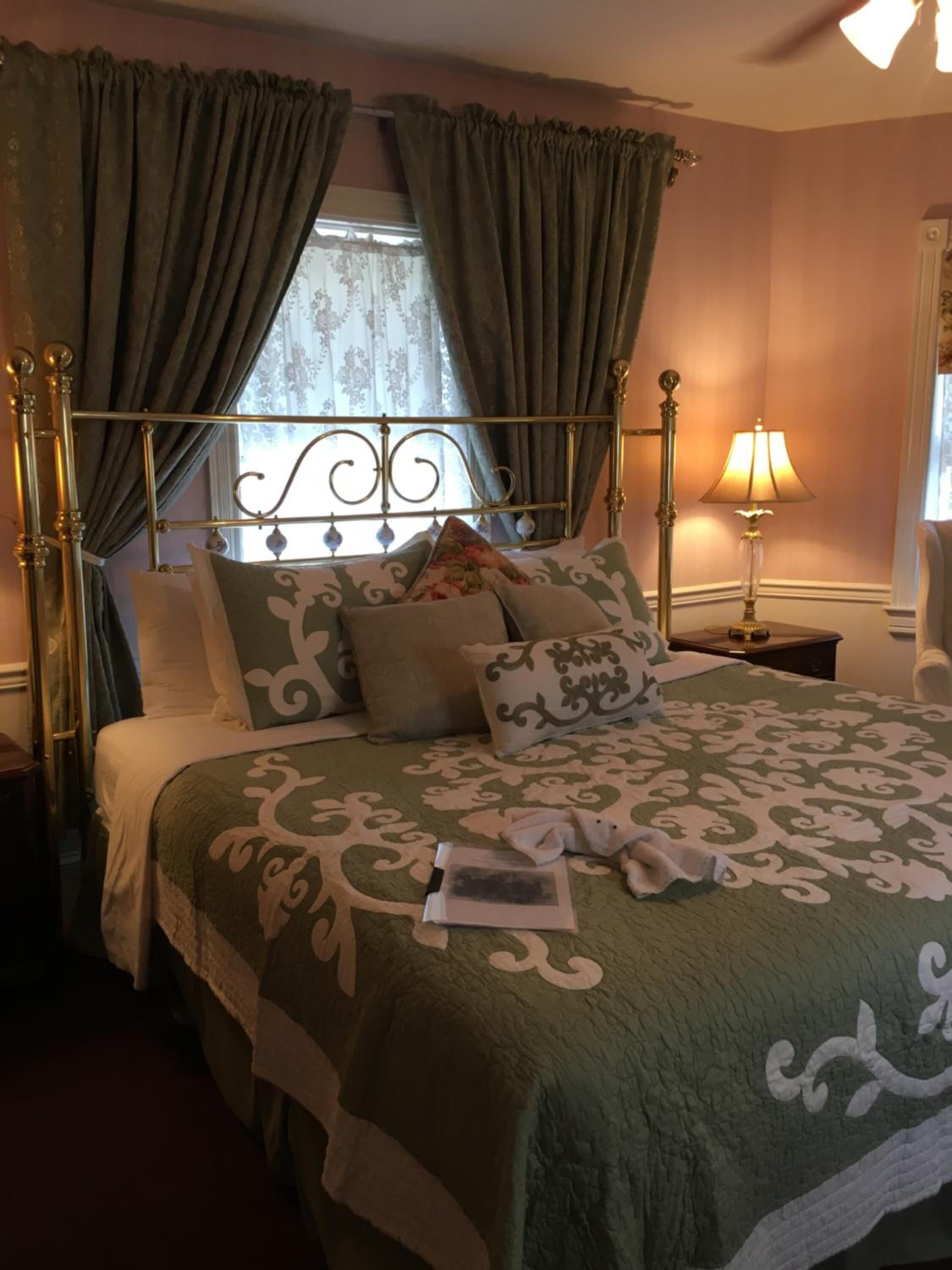 A neatly made bed with a green patterned bedspread, a metal headboard, and a bedside lamp.