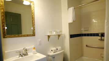 Un baño con lavamanos, inodoro y bañera. Hay un espejo con marco dorado y un estante sobre el inodoro.