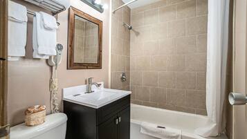 A bathroom with a white sink, dark cabinets, a mirror, a towel rack, and a shower with beige tiles.