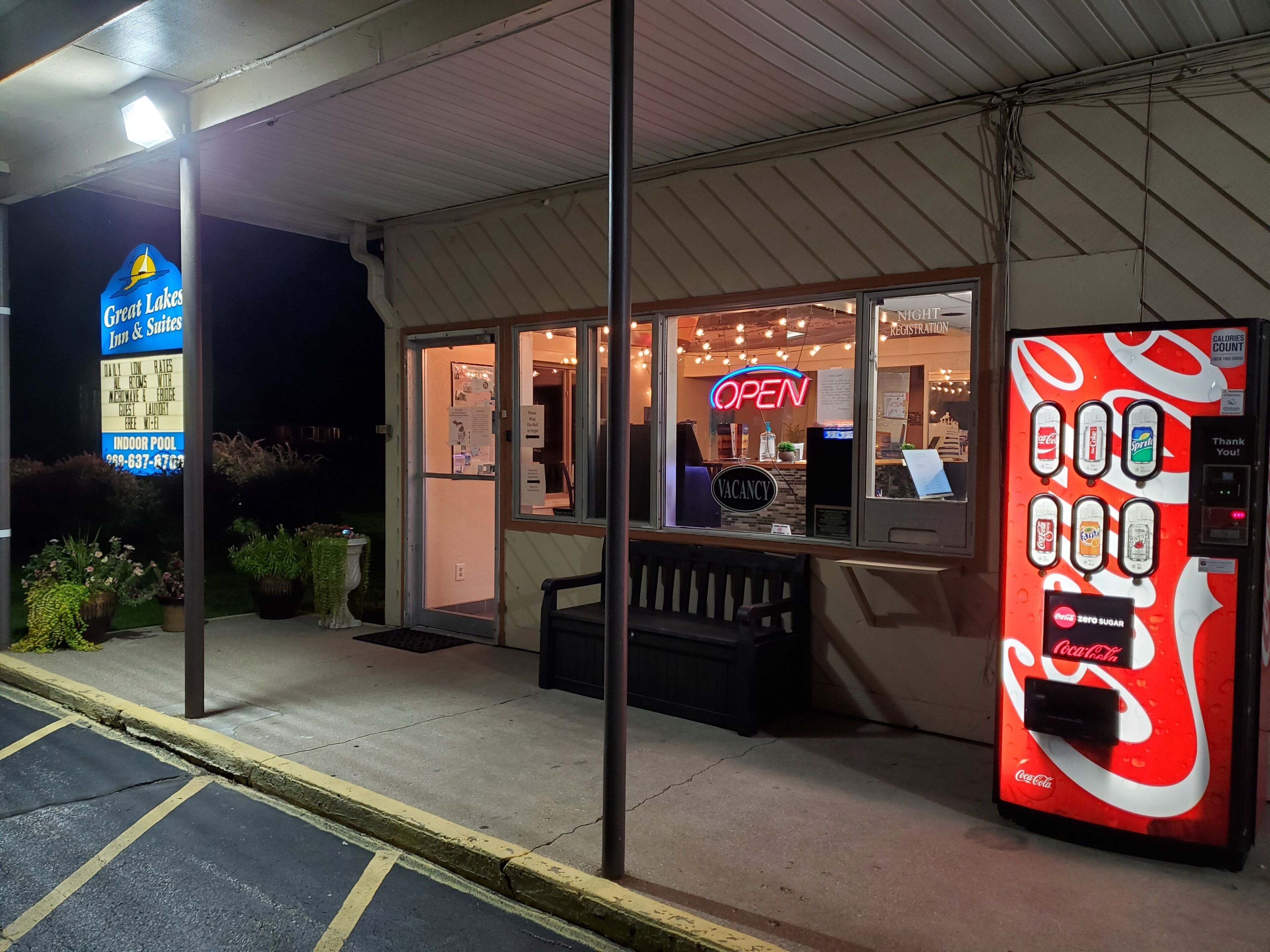 Entrada de hotel con una máquina expendedora de Coca-Cola y un letrero de neón que dice 'ABIERTO'.