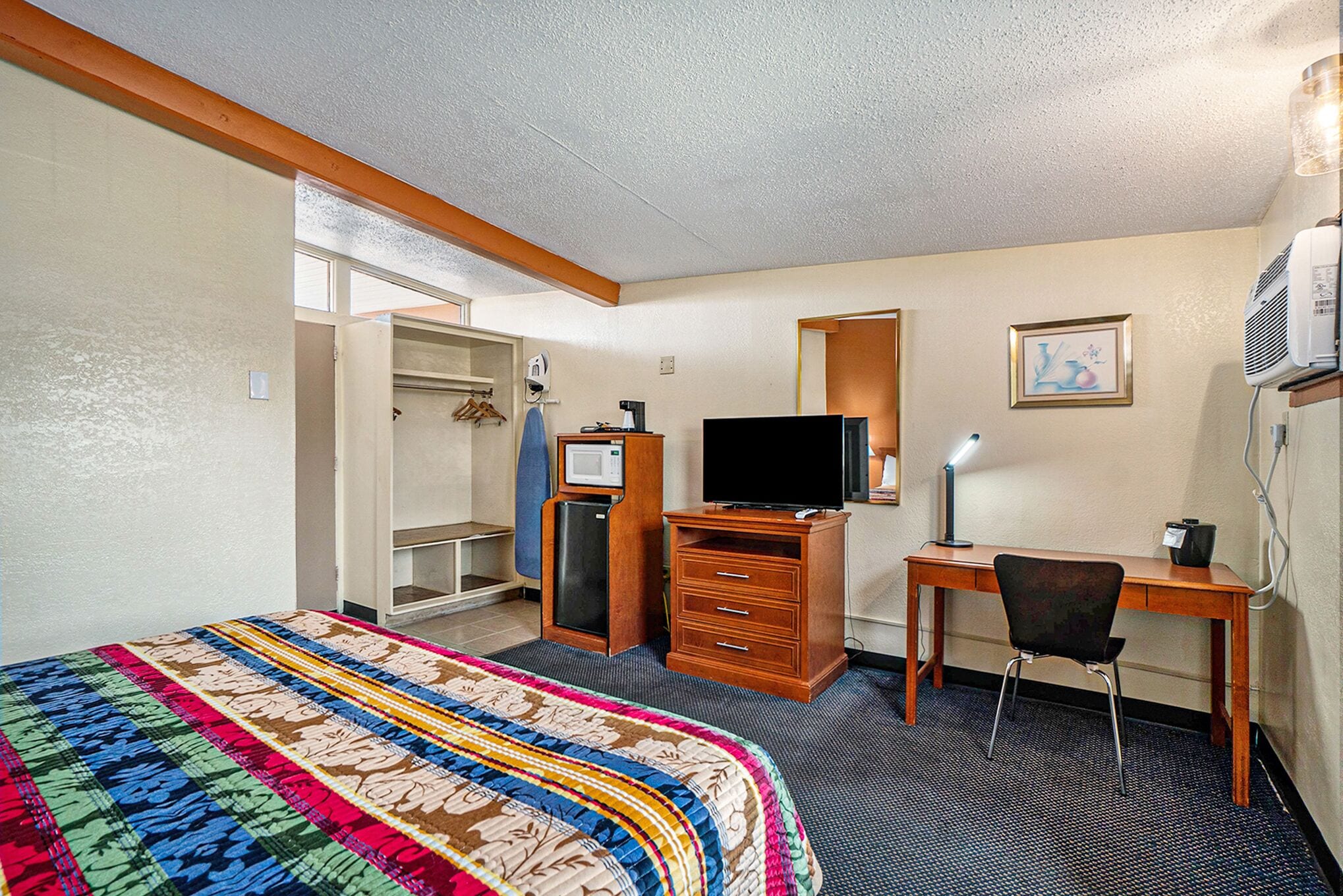 A hotel room with a bed, a desk, a chair, a television, a dresser, and a mirror.