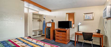 Een hotelkamer met een bed, een bureau, een stoel, een televisie, een kast en een spiegel.
