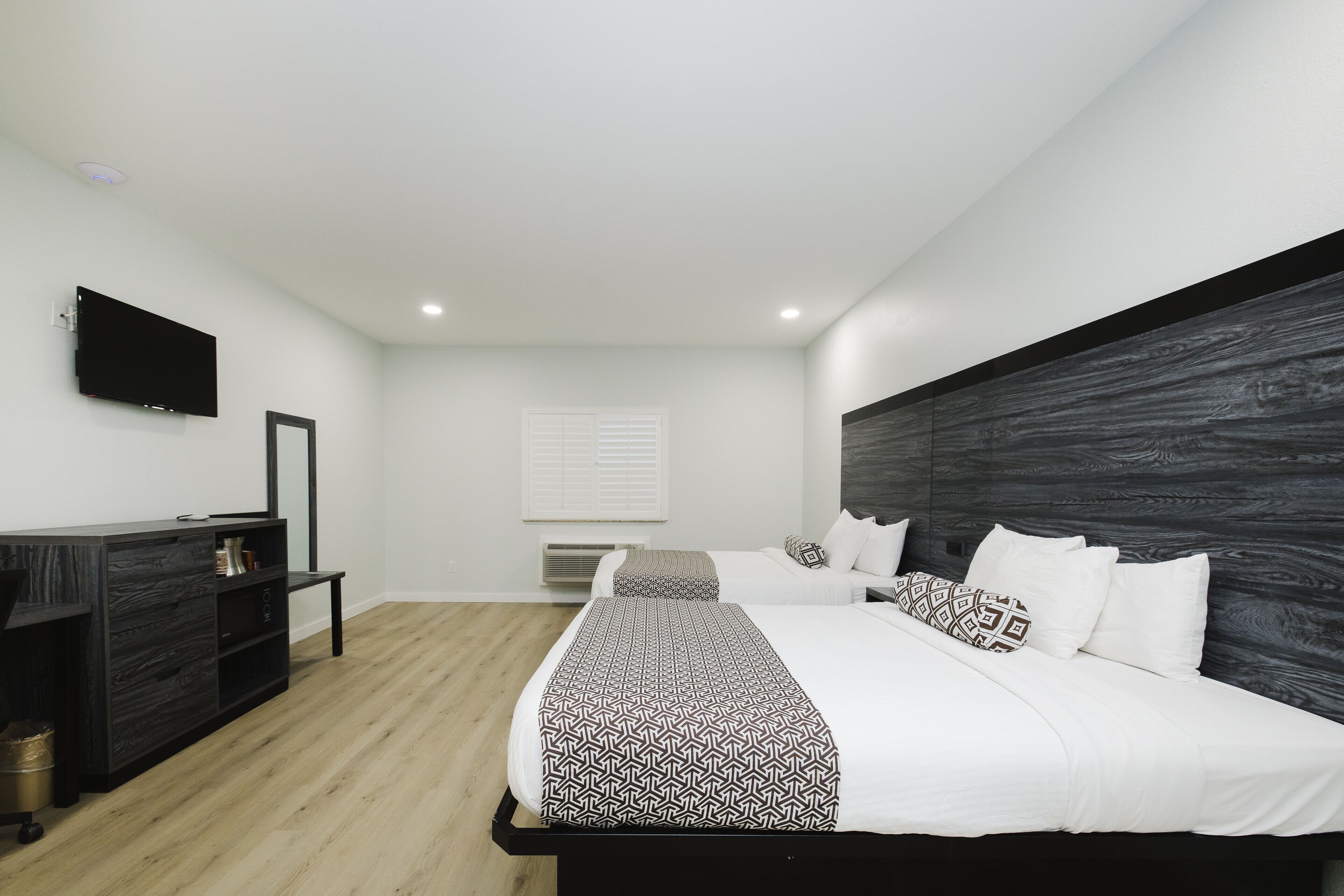 A modern bedroom with a large bed, a bedside table, a TV mounted on the wall, and a wooden headboard.