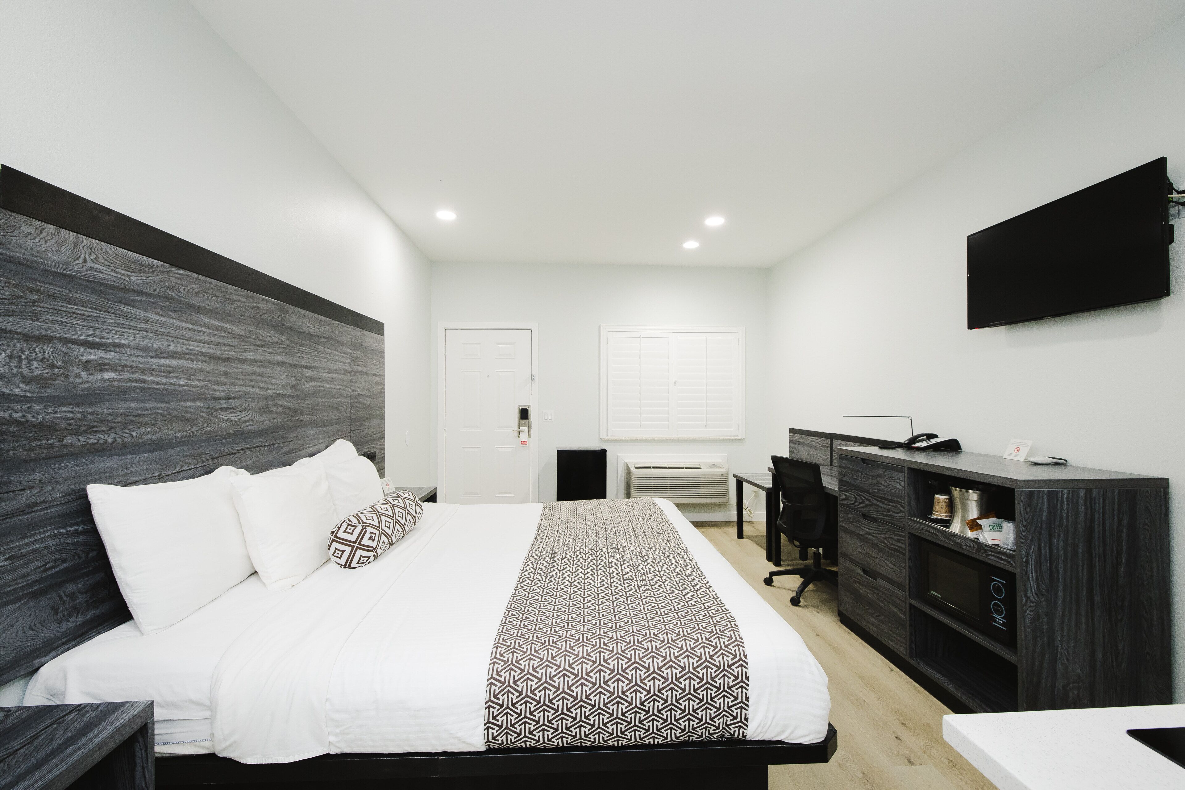A modern bedroom with a large bed, a desk, and a TV mounted on the wall.