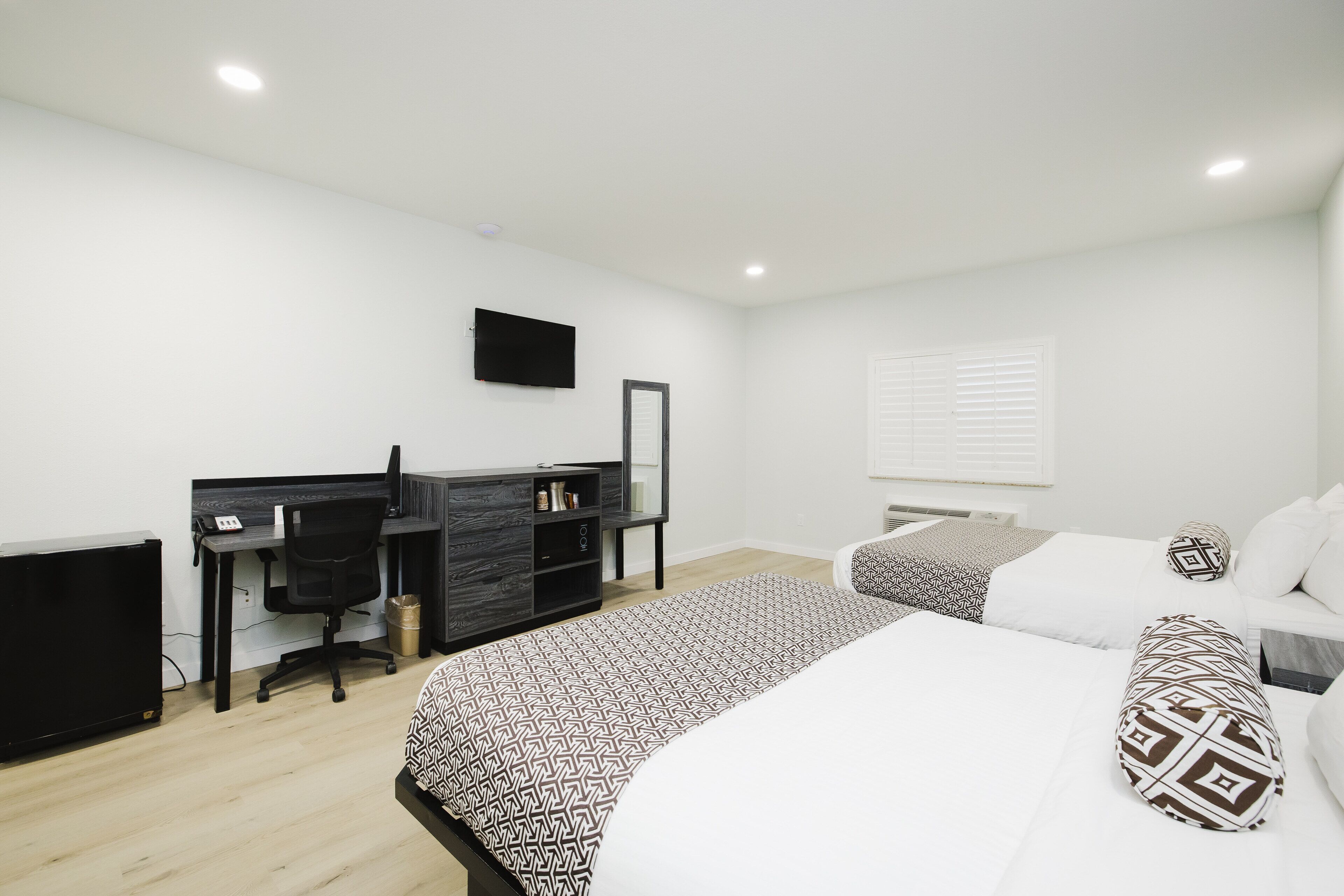 A modern bedroom with a desk, two beds, and a TV.