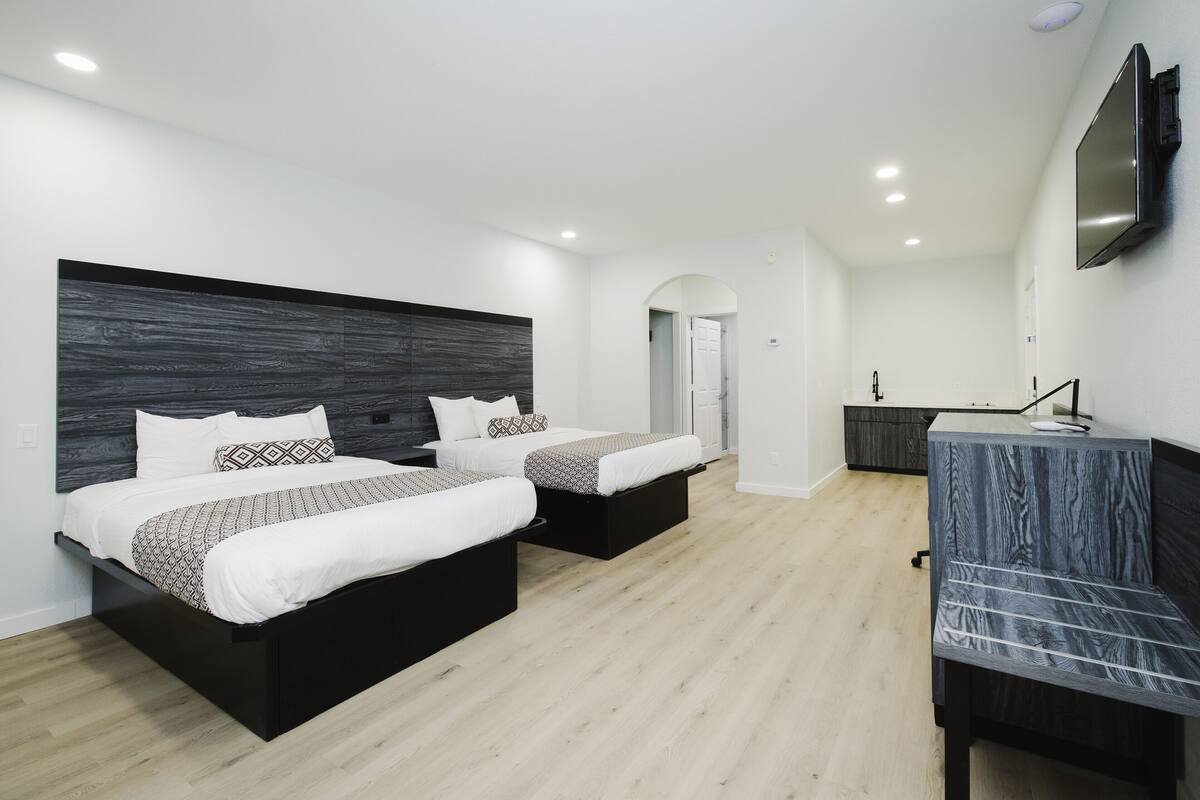 A modern bedroom with two beds, a desk, and a TV.