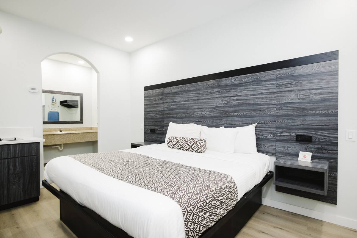 A modern bedroom with a large bed, a built-in nightstand, a vanity with a mirror, and a dark wood headboard.